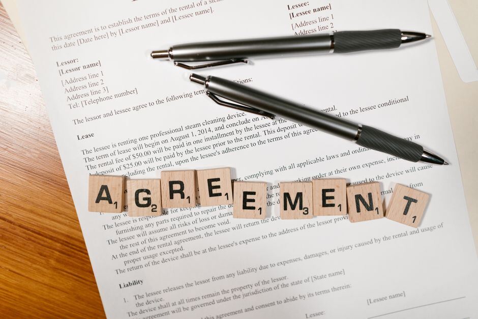 Letter tiles spelling agreement on a lease page beside two pens