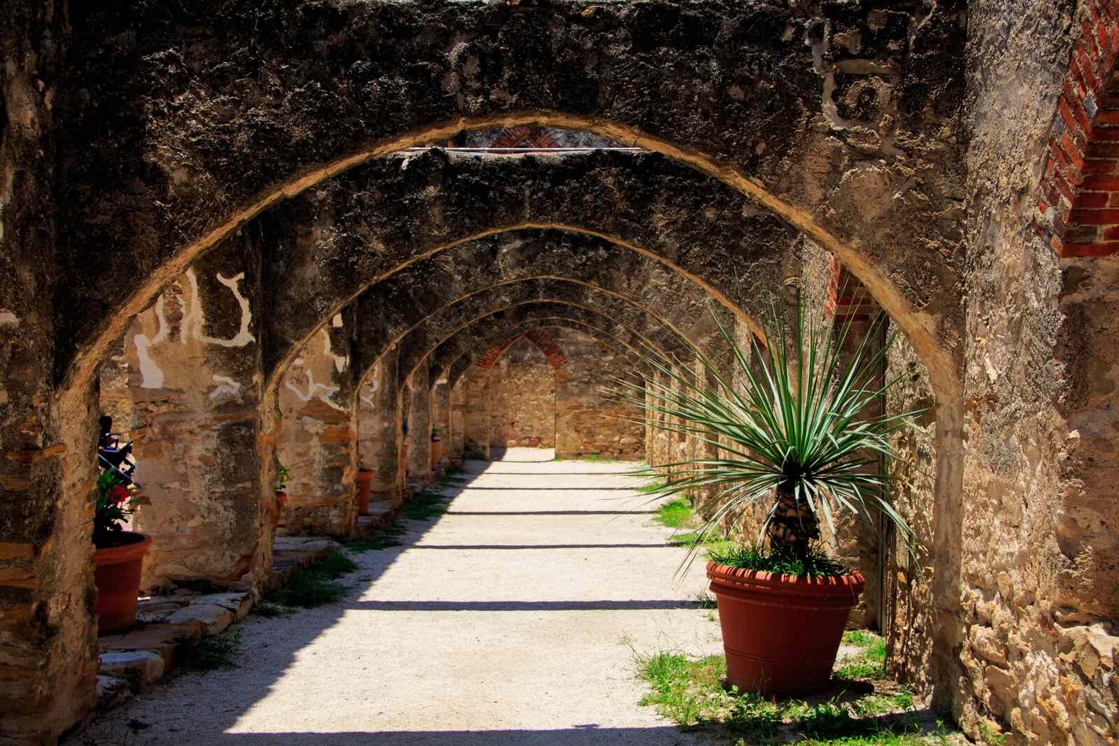 Arched stone walkway with potted plants at a San Antonio mission